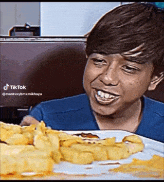 a boy is sitting at a table with a plate of french fries on it .