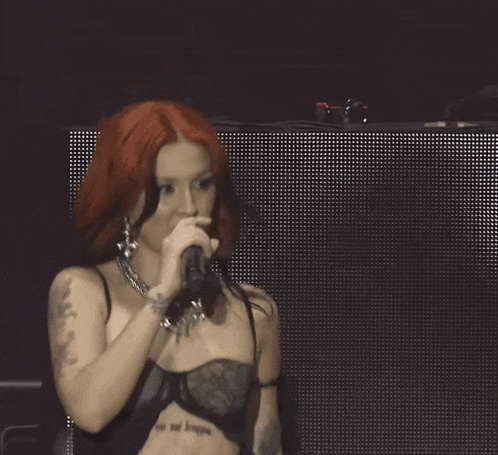 a woman with red hair singing into a microphone with a tattoo on her arm