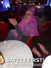 a man wearing a purple raincoat sits at a table with a bottle of whiskey