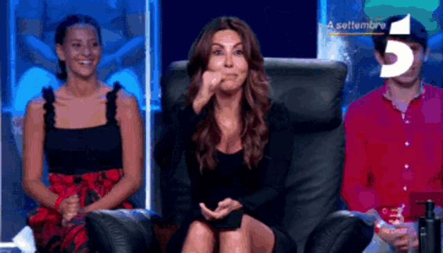 a woman in a black dress is sitting in a chair in front of a sign that says " a settembre 5 "