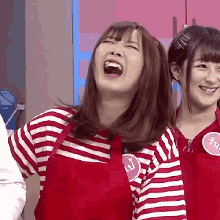 a woman wearing an apron is laughing while standing next to another woman wearing a striped shirt .