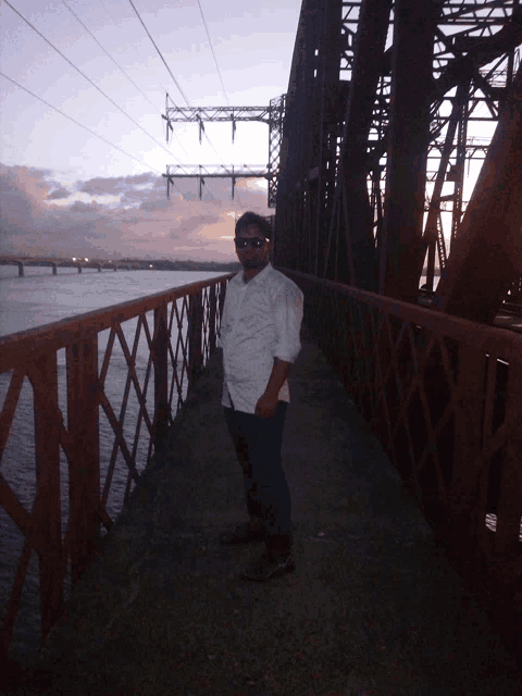 a man in a white shirt stands on a bridge over a body of water