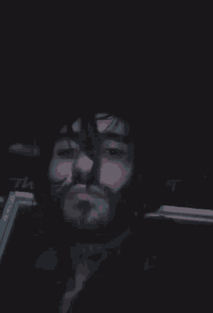 a man with a beard is smoking a cigarette in a dark room .