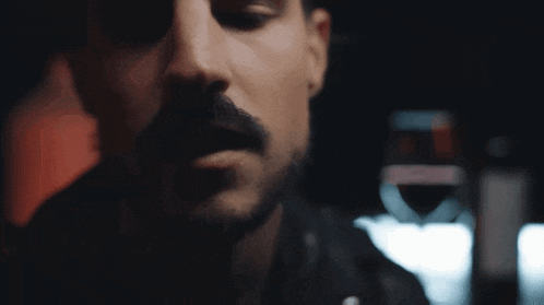a close up of a man 's face with a glass of wine in the background .