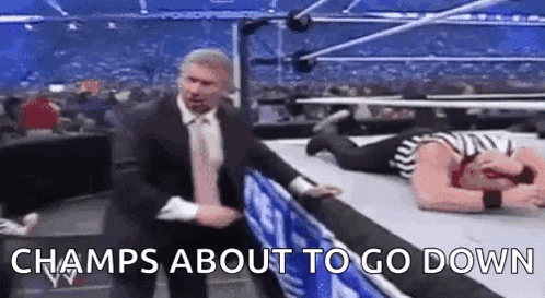 a man in a suit and tie is standing next to a wrestler who is laying on the floor .