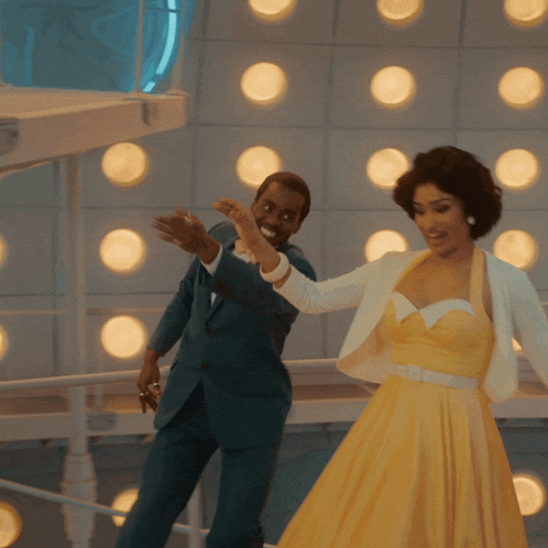 a man in a suit and woman in a yellow dress are dancing