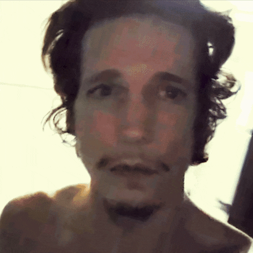 a man without a shirt has a beard and looks at the camera