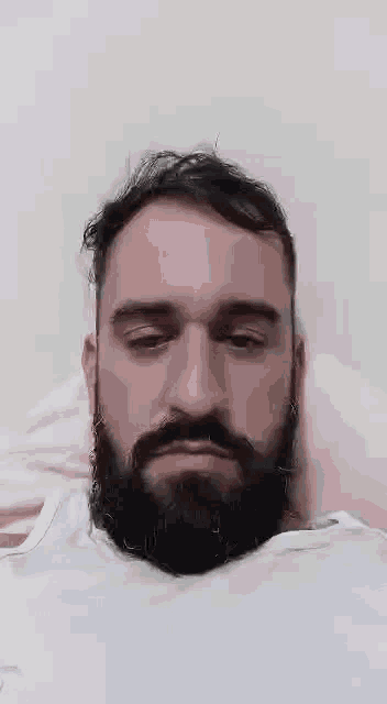 a man with a beard is laying on a bed and making a face .