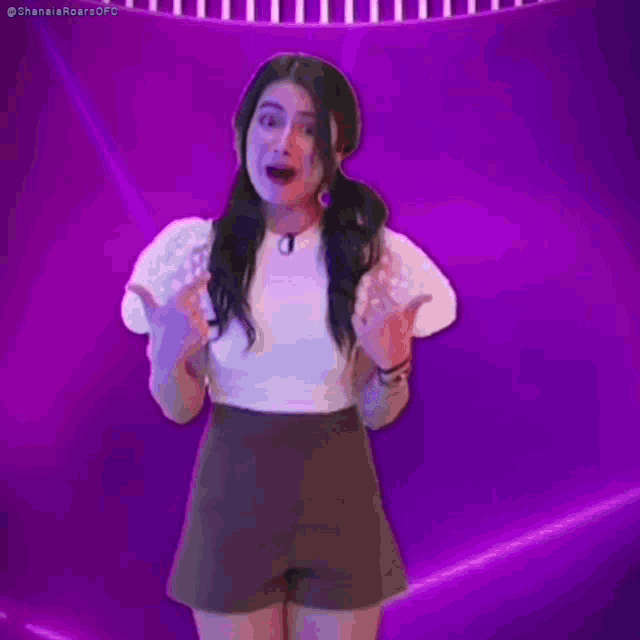 a woman in a white top and brown shorts is laughing while standing in front of a purple background .