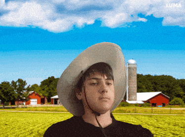 a young man wearing a cowboy hat is standing in front of a farm