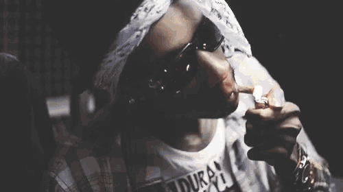 a man wearing a bandana and sunglasses lighting a cigarette