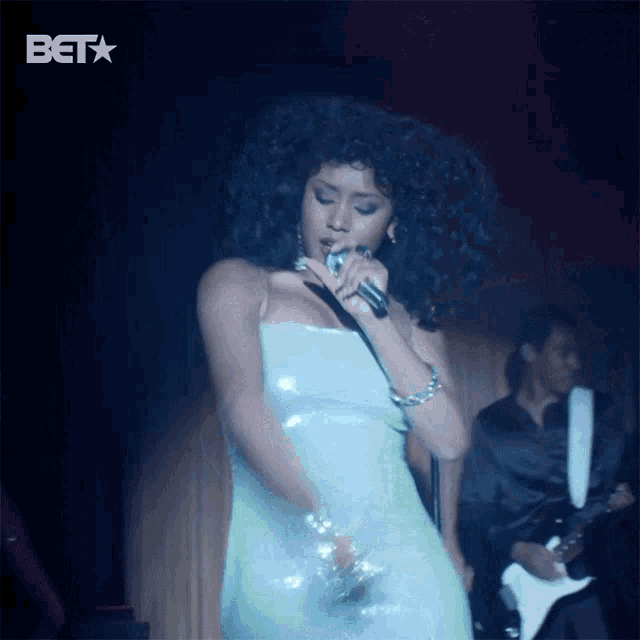 a woman in a green dress is singing into a microphone with a bet logo behind her