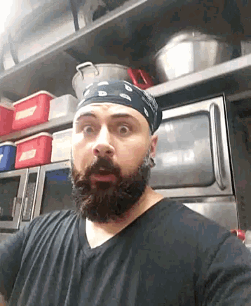 a man with a beard wearing a bandana is standing in a kitchen