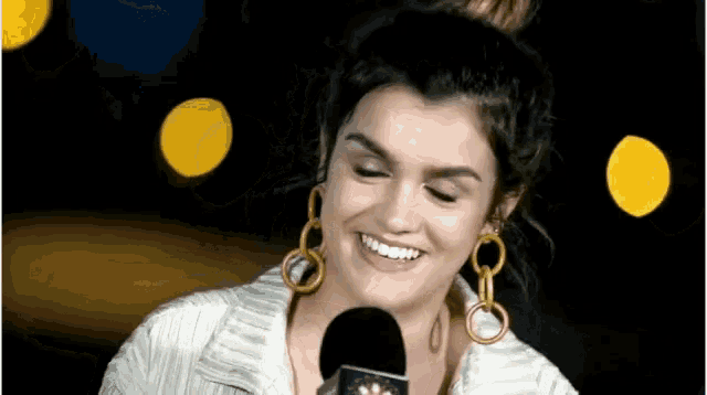 a woman wearing gold earrings is smiling into a microphone .