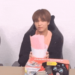 a young man is sitting at a table holding a box of mario kart remote control .