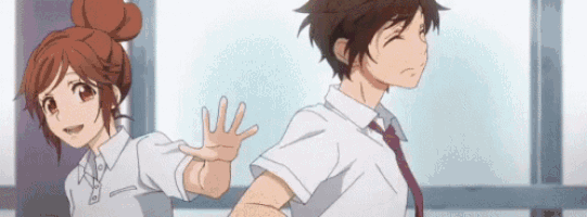 a boy and a girl are standing next to each other in a room . the girl is waving at the boy .