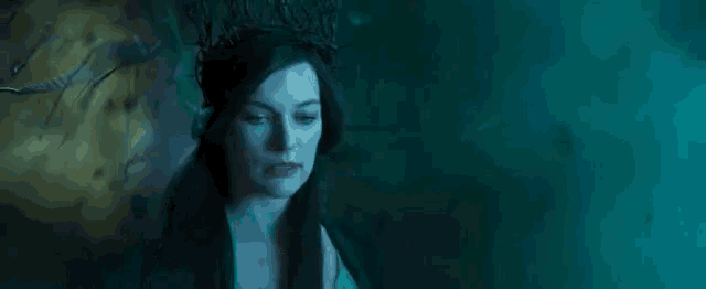 a woman wearing a crown of branches on her head is standing in a dark room .