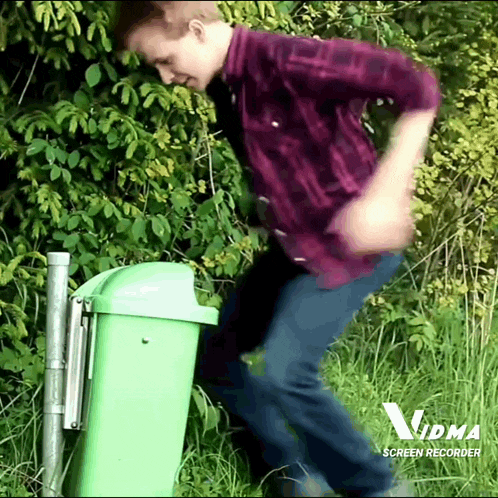 a man in a plaid shirt is standing next to a green trash can that says vdma screen recorder on it
