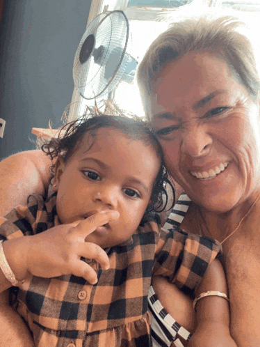 a woman holds a baby in her arms and the baby is wearing a plaid shirt