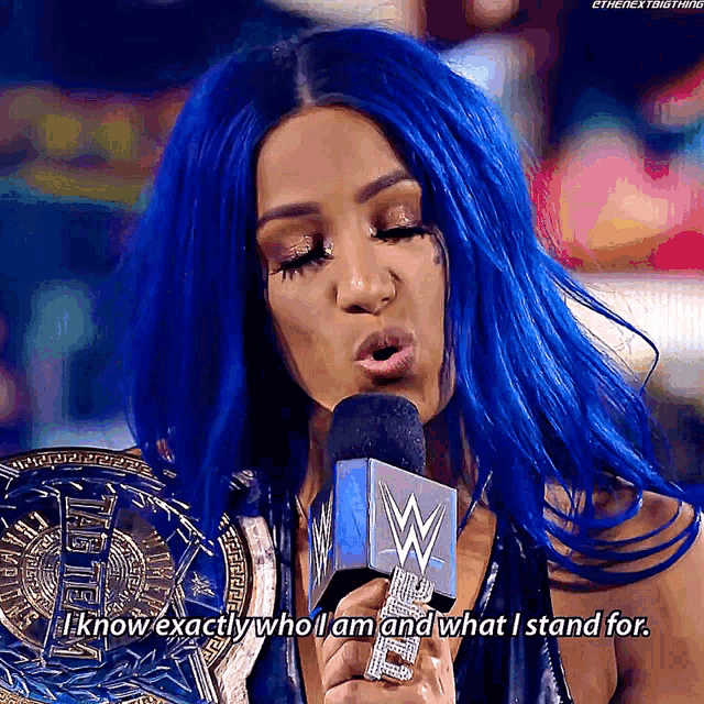 a woman with blue hair is speaking into a microphone and says " i know exactly who i am and what i stand for "