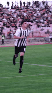 a soccer player wearing a black and white striped jersey is running on the field