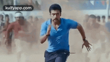 a man in a blue shirt and black pants is running on a dirt road .