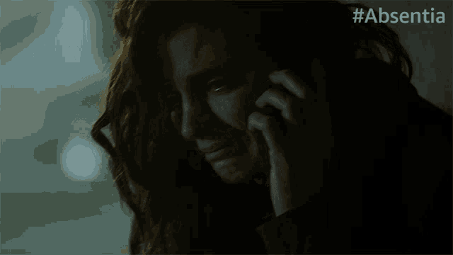 a woman is crying while talking on a phone with #absentia written on the bottom right