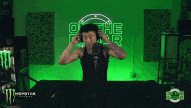 a man wearing headphones stands in front of a green monster energy sign