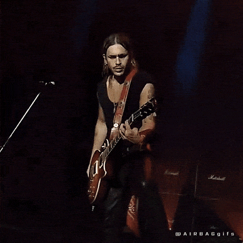 a man with long hair is playing a guitar in front of a microphone