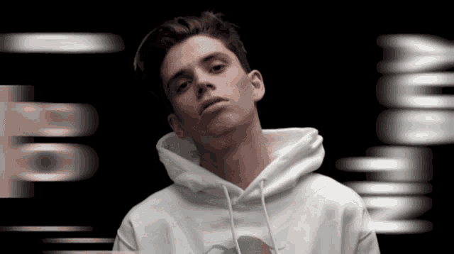 a young man wearing a white hoodie stands in front of a blurred background