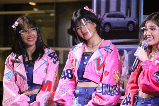 three girls wearing pink jackets with the number 48 on them stand in front of a microphone