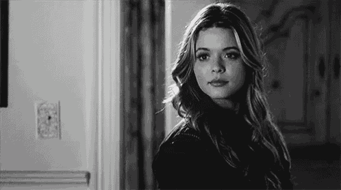 a black and white photo of a woman looking at the camera in a hallway .