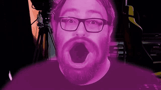 a man with glasses and a beard is making a surprised face with his mouth wide open .