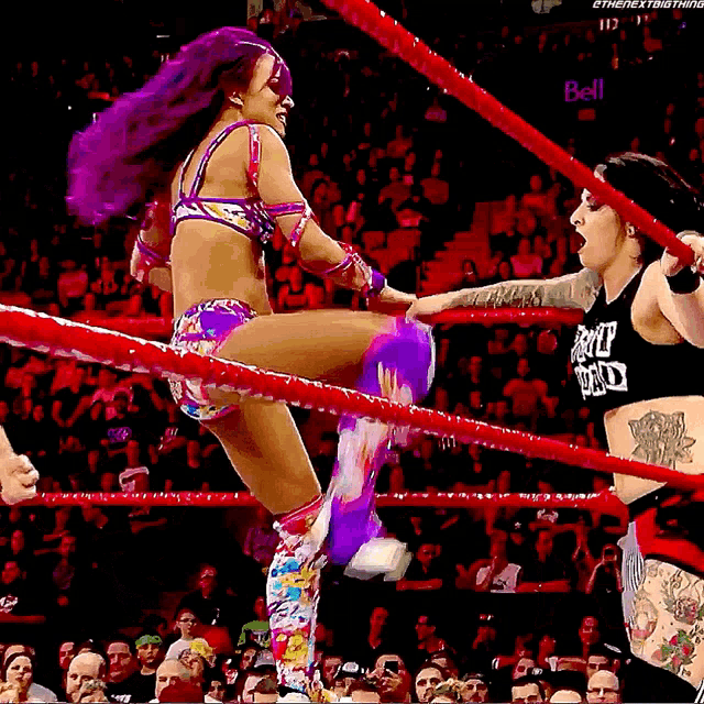 a female wrestler with purple hair is kicking another wrestler in a ring that says bell