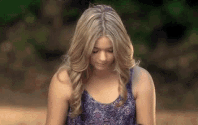 a woman in a purple tank top is standing on a dirt road looking down .