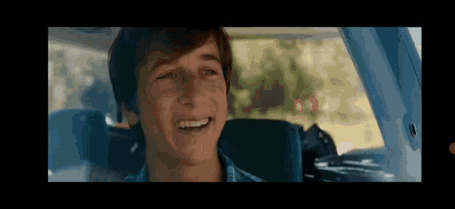 a young man is sitting in the driver 's seat of a car and smiling .