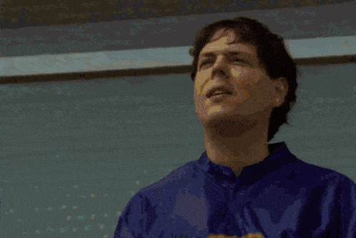 a man in a blue shirt is standing on a balcony looking out the window