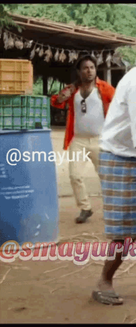a man in a red jacket is standing in front of a blue barrel with the hashtag smayurt
