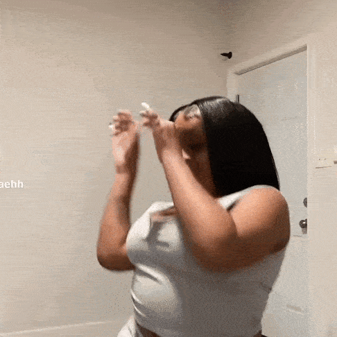 a woman in a white tank top is standing in a room with her hands up .