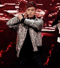a man in a black and white jacket is standing on a stage with his arms crossed