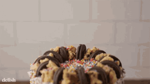 a cake with oreos and sprinkles has the word delish on the bottom right