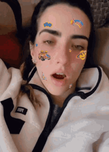 a woman with stickers on her face is wearing a white jacket with the letter r on the front