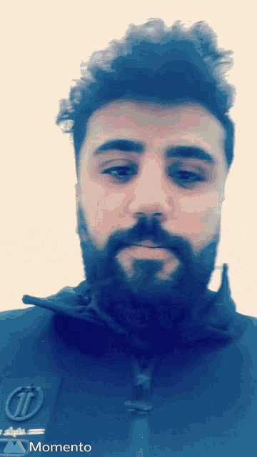 a man with a beard wearing a momento jacket looks at the camera