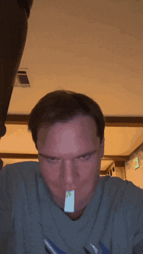 a man in a grey shirt has a piece of paper in his mouth with a smiley face on it