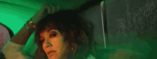 a woman is sitting in a dark room with a green light behind her and touching her hair .
