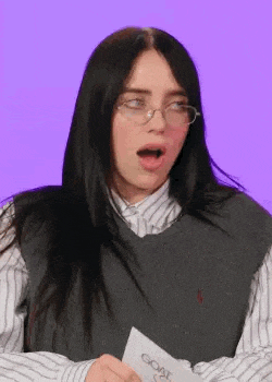 billie eilish is wearing glasses and a striped shirt and holding a piece of paper .