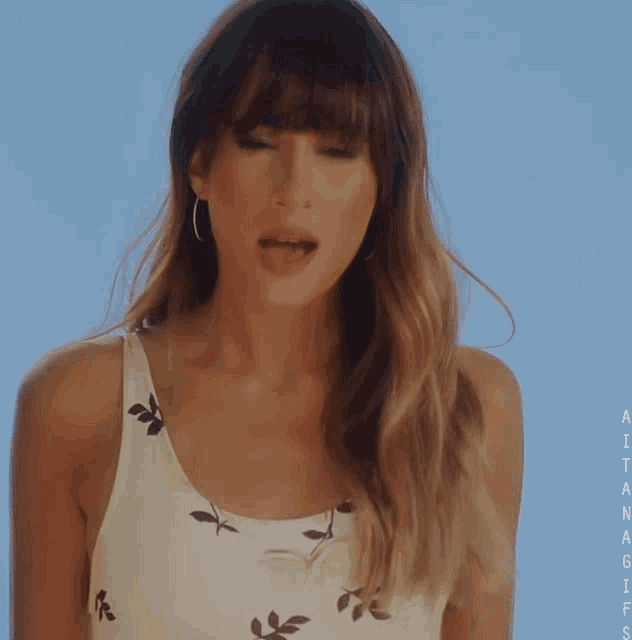 a woman wearing a white tank top with leaves on it is singing