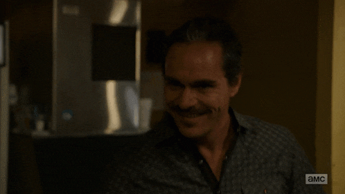 a man with a mustache is smiling in front of a wall that says a.m.c.
