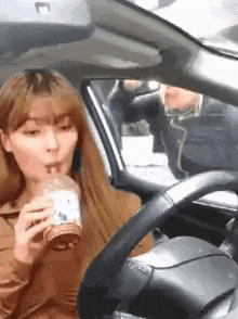 a woman is sitting in a car drinking a cup of coffee .
