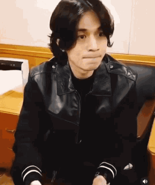 a man with long hair is sitting in a chair wearing a black leather jacket .